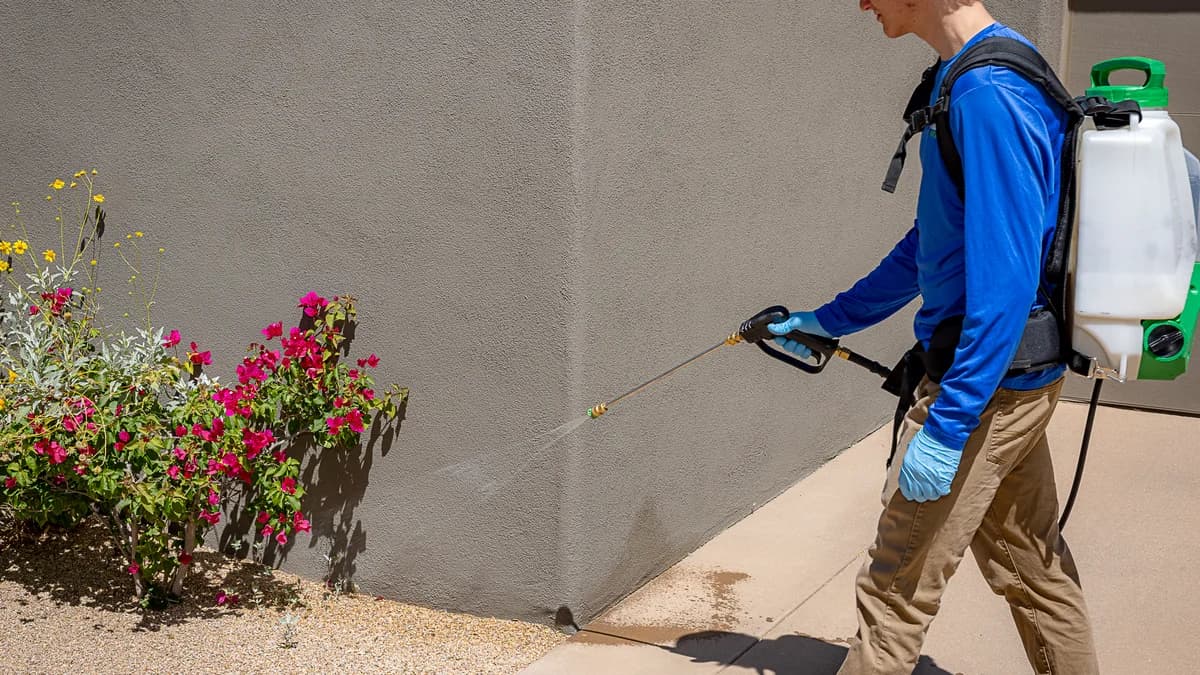 A pest control technician treating the exterior perimeter of a Phoenix-area home