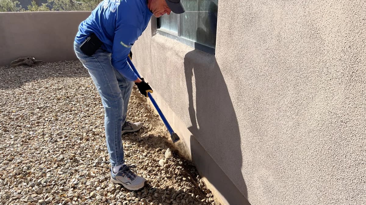A pest control technician treating the block wall and landscape rock at the perimeter of an Arizona home